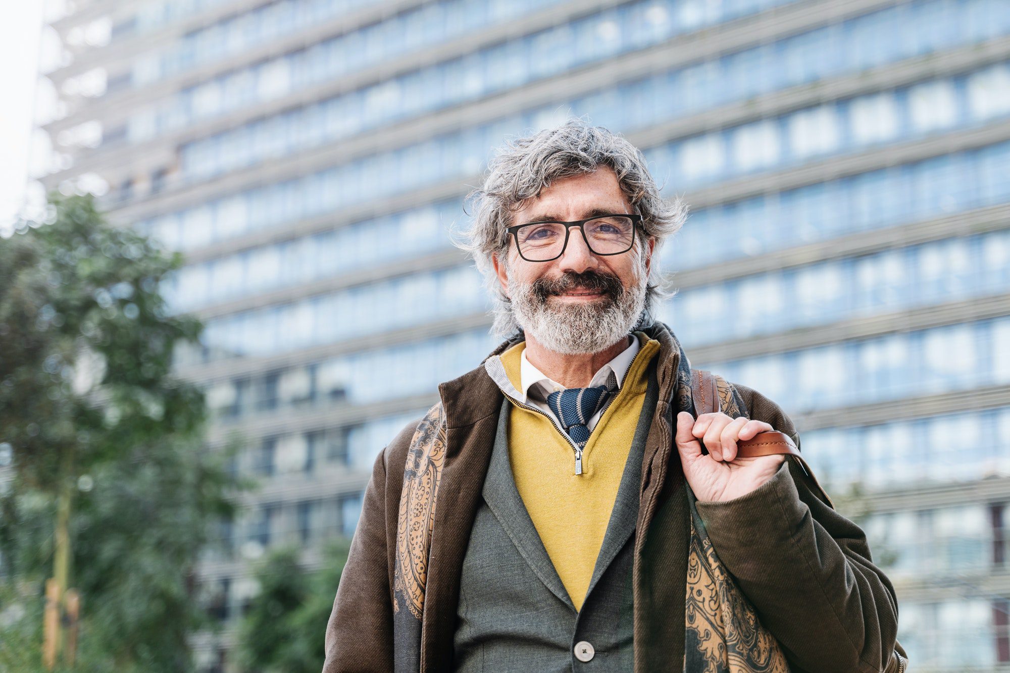 Happy elegant senior man with grey beard and eyeglasses outside the company office